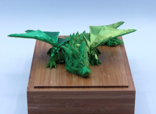 Filmbeli 3D nyomtatott kicsi sárkány figura, zöld színben kis szárnyakkal.